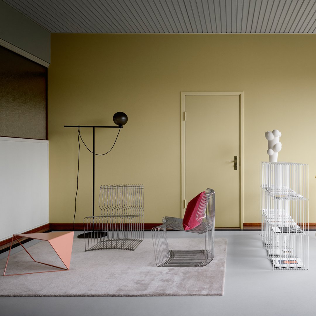 "Pastel pink and grey patterns with transparent acrylic furniture against a muted yellow wall."