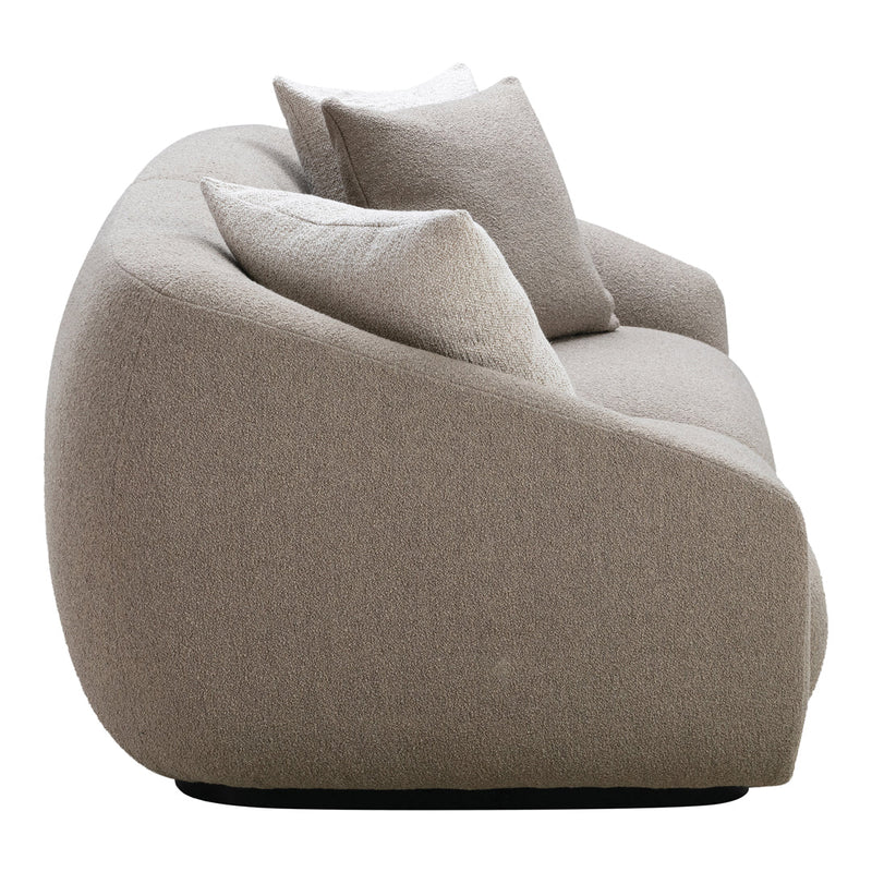 Curved beige sofa with textured fabric and soft white pillows, featuring a minimalist design and neutral color palette.
