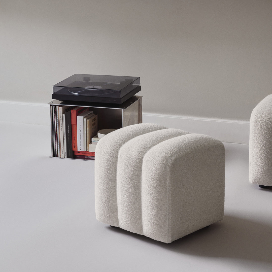 Cream-colored upholstered stool with a ribbed pattern, set against a minimalist backdrop.