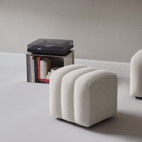 Cream-colored upholstered stool with a ribbed pattern, set against a minimalist backdrop.