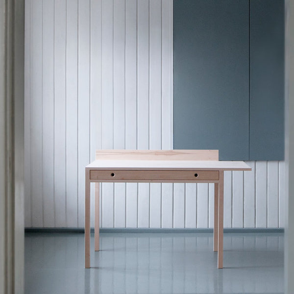Light natural wood table with minimalistic design, set against a soft gray background and white vertical paneling.
