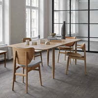Light wood dining table with natural finish, complemented by beige upholstered chairs in a modern, minimalist setting.