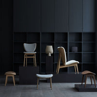 Stylish chairs in muted gray and beige tones, set against a bold black backdrop with clean lines and modern patterns.