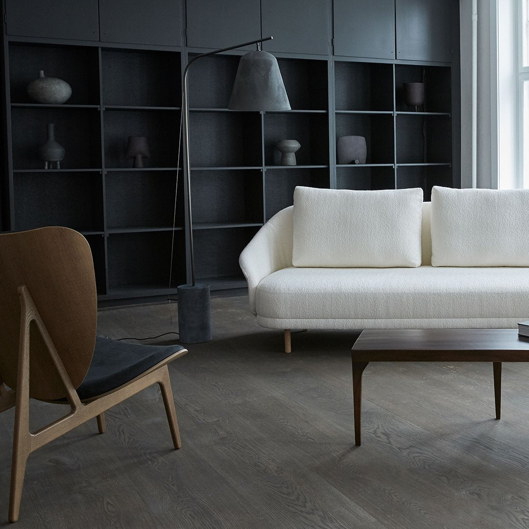 "Modern white sofa with subtle texture, paired with a warm brown chair in a minimalist black and gray setting."