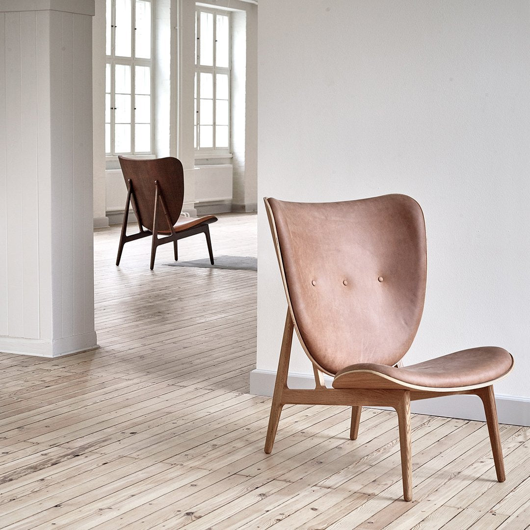 Copper-toned leather chair with a smooth, minimalist design and subtle tufted pattern, set against a light wooden floor.