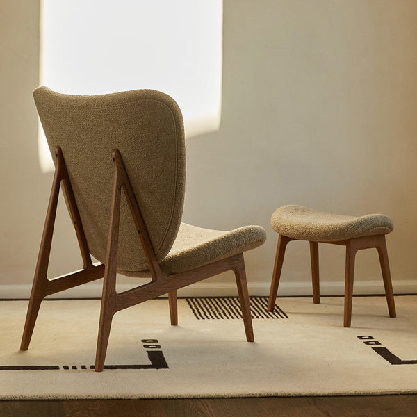 Beige upholstered chair with wooden legs, paired with a matching footstool on a simple patterned cream rug.