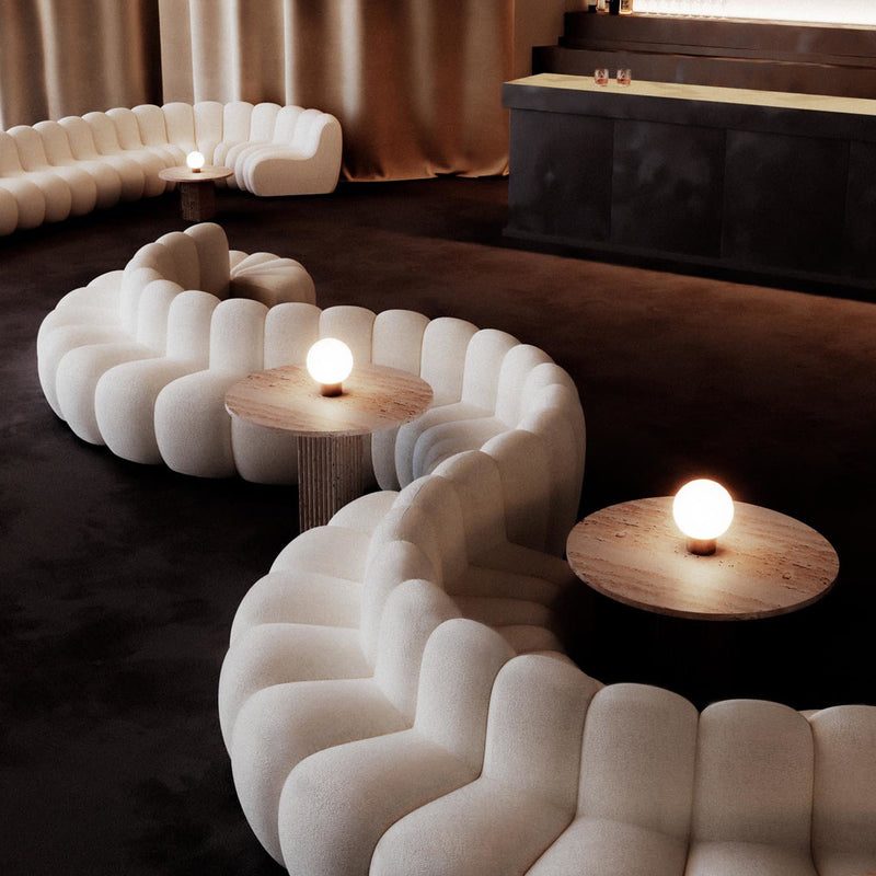Curved white lounge seating with soft, textured patterns, set against a dark brown floor and warm lighting.