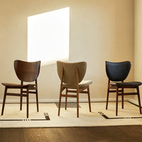 Three stylish chairs in dark wood, light beige, and deep blue, arranged on a modern patterned rug under soft lighting.