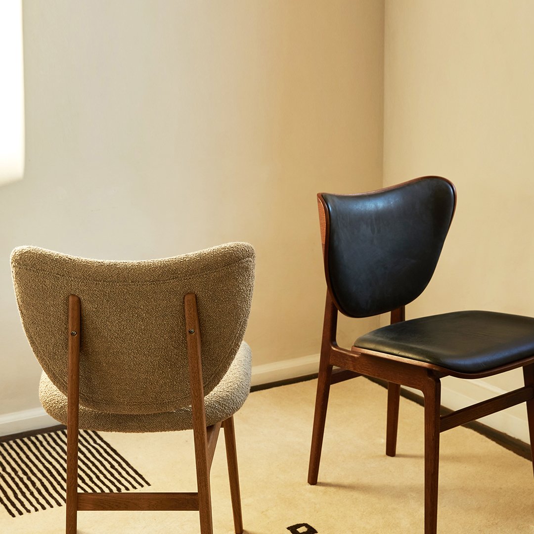 Two mid-century style chairs: one in soft gray upholstery and the other in sleek black leather with wooden legs.