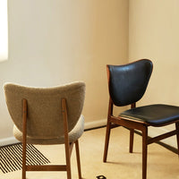 Two mid-century style chairs: one in soft gray upholstery and the other in sleek black leather with wooden legs.