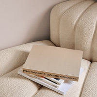 Neutral beige book resting on white stacked books, against a textured cream-colored sofa for a minimalist aesthetic.