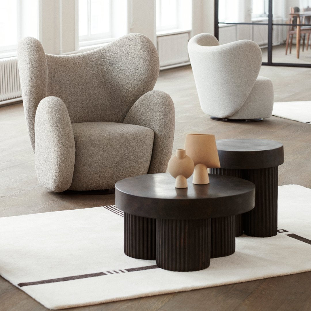 Gray upholstered armchair with a modern, rounded shape; dark wood accent tables on a light rug.