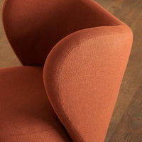 Rust-colored upholstered chair with a smooth, textured finish and curved armrests against a wooden floor backdrop.