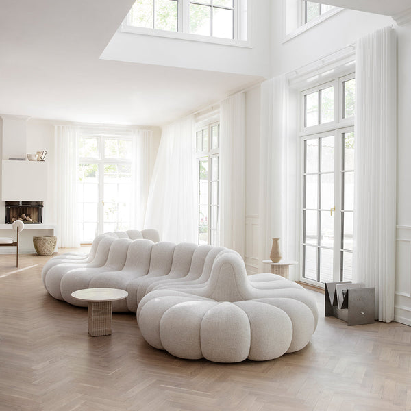 White, plush sofa with a rounded, cloud-like design in a bright, airy room featuring light wood flooring and large windows.