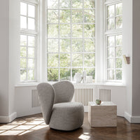 Gray upholstered chair with a sleek, modern design, positioned next to a light-colored square table in a bright setting.
