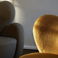 Two modern chairs in warm gray and rich mustard colors with textured, fuzzy upholstery against a soft-lit background.