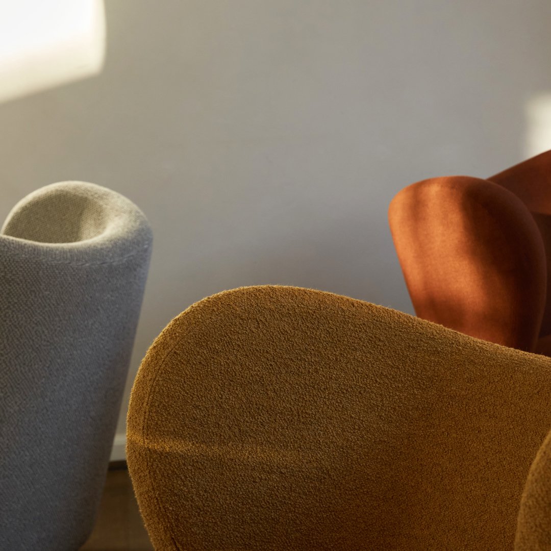 Soft gray, warm rust, and rich mustard chairs with smooth, rounded contours against a neutral backdrop.