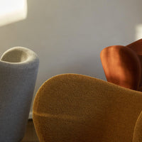 Soft gray, warm rust, and rich mustard chairs with smooth, rounded contours against a neutral backdrop.