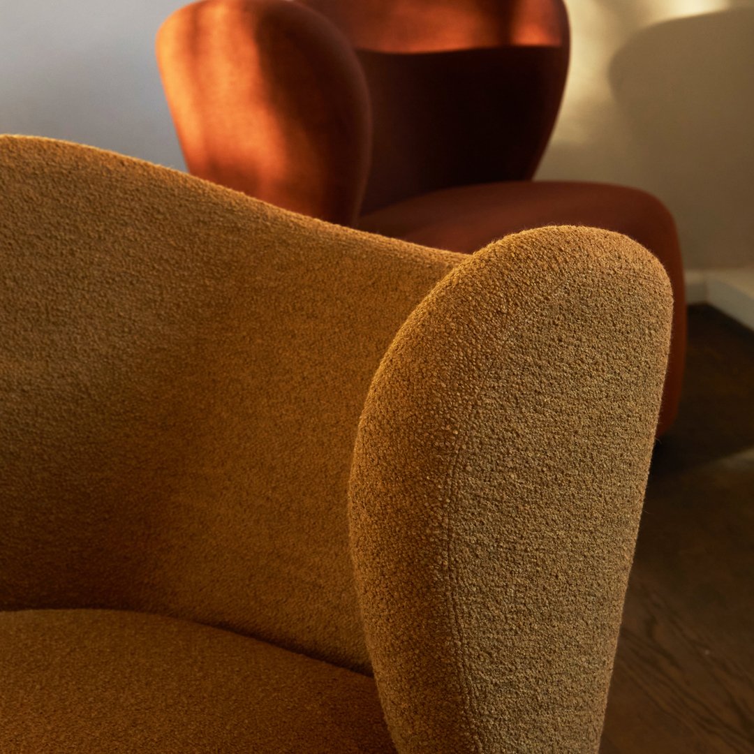"Textured brown chair in foreground, warm red chair softly lit in background, showcasing stylish modern design."