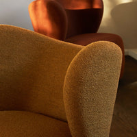 "Textured brown chair in foreground, warm red chair softly lit in background, showcasing stylish modern design."
