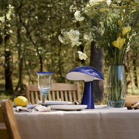 "Elegant outdoor dining setup with a blue lamp, transparent glassware, and vibrant yellow flowers."