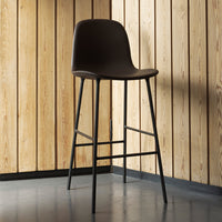 Dark brown bar stool with sleek black metal legs against a warm, natural wood panel background. Modern and minimalist design.