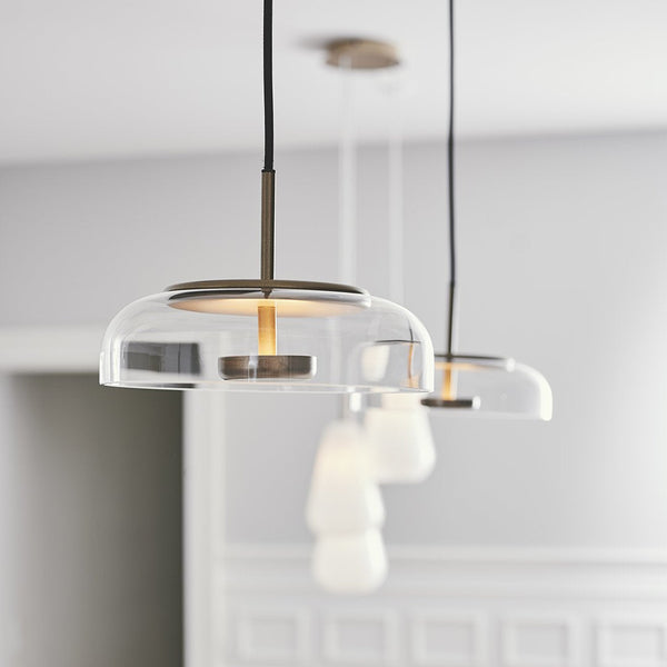 Clear glass pendant lights with soft white shades and a sleek black cord. Elegant, modern design in a neutral setting.