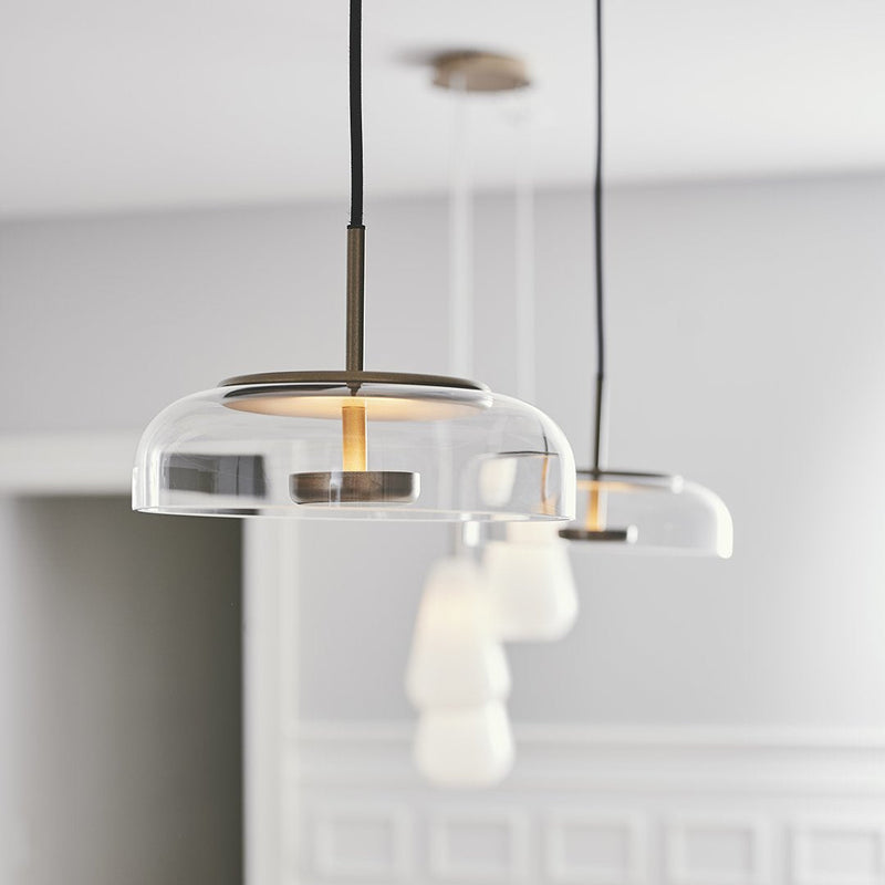 Clear glass pendant lights with soft white shades and a sleek black cord. Elegant, modern design in a neutral setting.