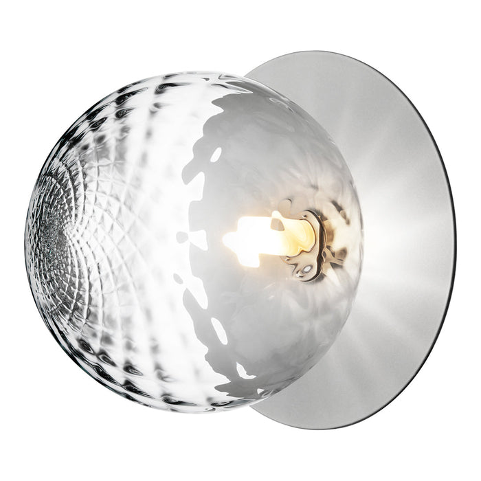 "Modern silver wall lamp with a textured, clear glass globe and polished chrome backing, creating a stylish light pattern."