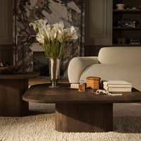Brown wooden coffee table with a smooth surface, surrounded by light beige and textured area rug, accented with white flowers.