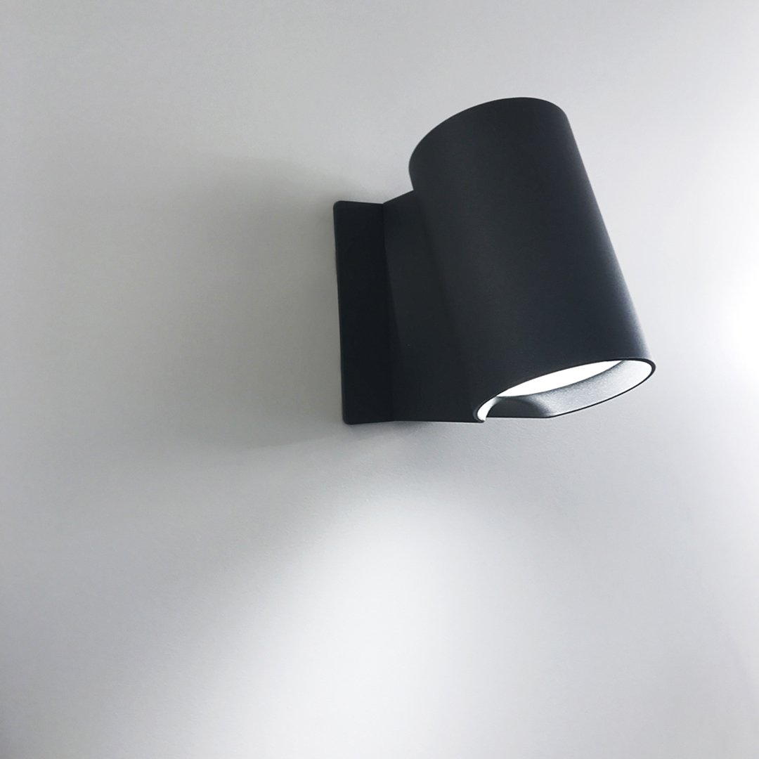 Sleek black wall lamp with a minimalist design, featuring a smooth matte finish and a cylindrical shade.