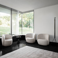 Modern living room featuring soft beige armchairs, a sleek black table, and a light rug on dark flooring. Bright natural light.