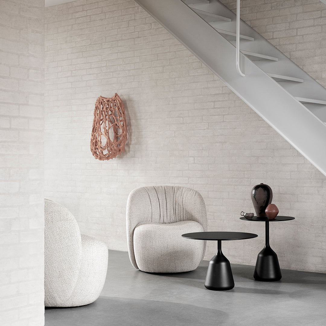 Neutral textured chairs with a soft white finish, black side tables, and a decorative rose gold wall piece.