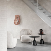 Neutral textured chairs with a soft white finish, black side tables, and a decorative rose gold wall piece.
