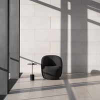 Modern black armchair with a textured pattern against a light stone wall, casting geometric shadows.