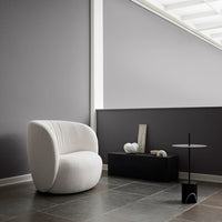 Circular white accent chair against a muted gray wall, with sleek black furniture and stone-tiled floor.