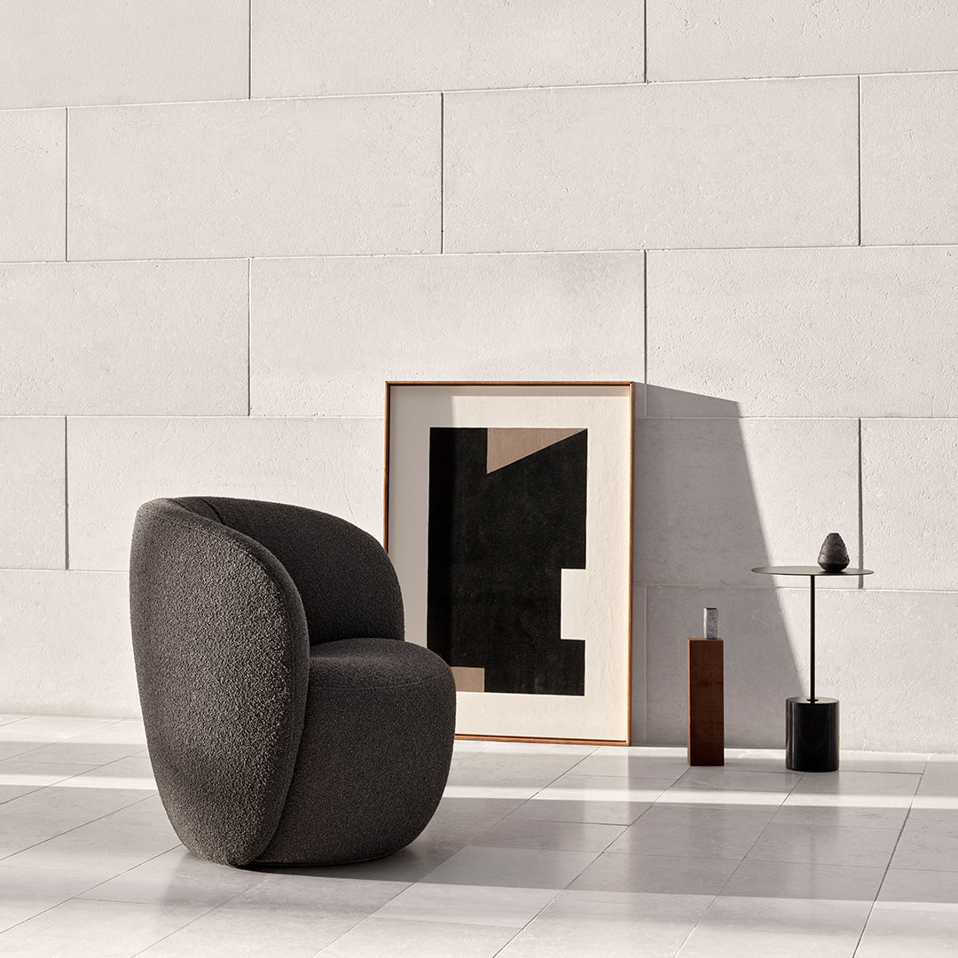 Textured dark gray chair against a minimalist light wall, complemented by abstract black and beige artwork.
