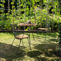 Outdoor bistro set featuring black metal frames and wooden seats, surrounded by greenery and natural light.