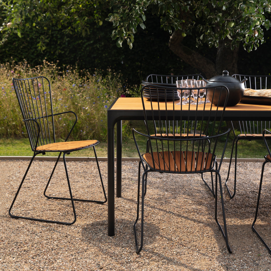 Black metal outdoor chairs with wooden seats around a matching table, set against a natural, green backdrop.