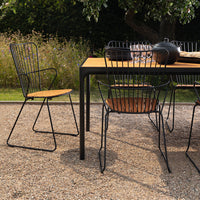 Stylish black wire patio chairs with natural wood seats, paired with a matching black and wood table in a garden setting.