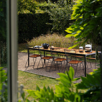 "Outdoor dining set featuring sleek black metal and warm wooden accents, surrounded by lush greenery."