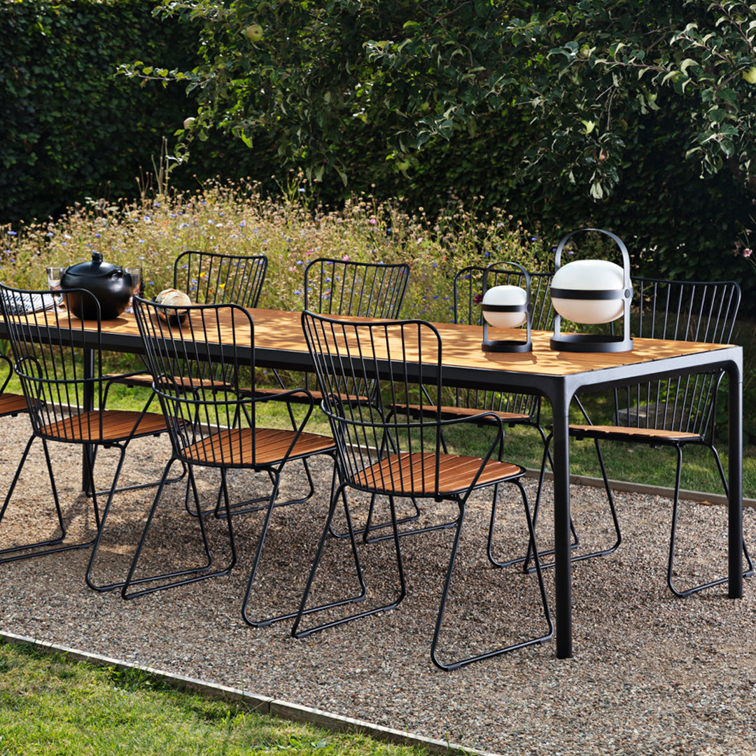 Stylish outdoor dining set featuring a wooden tabletop, black wire chairs, and a modern ceramic lantern. Perfectly balanced colors.