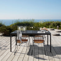 "Black outdoor dining table with striped cushions and wicker chairs, set against a scenic coastal backdrop."