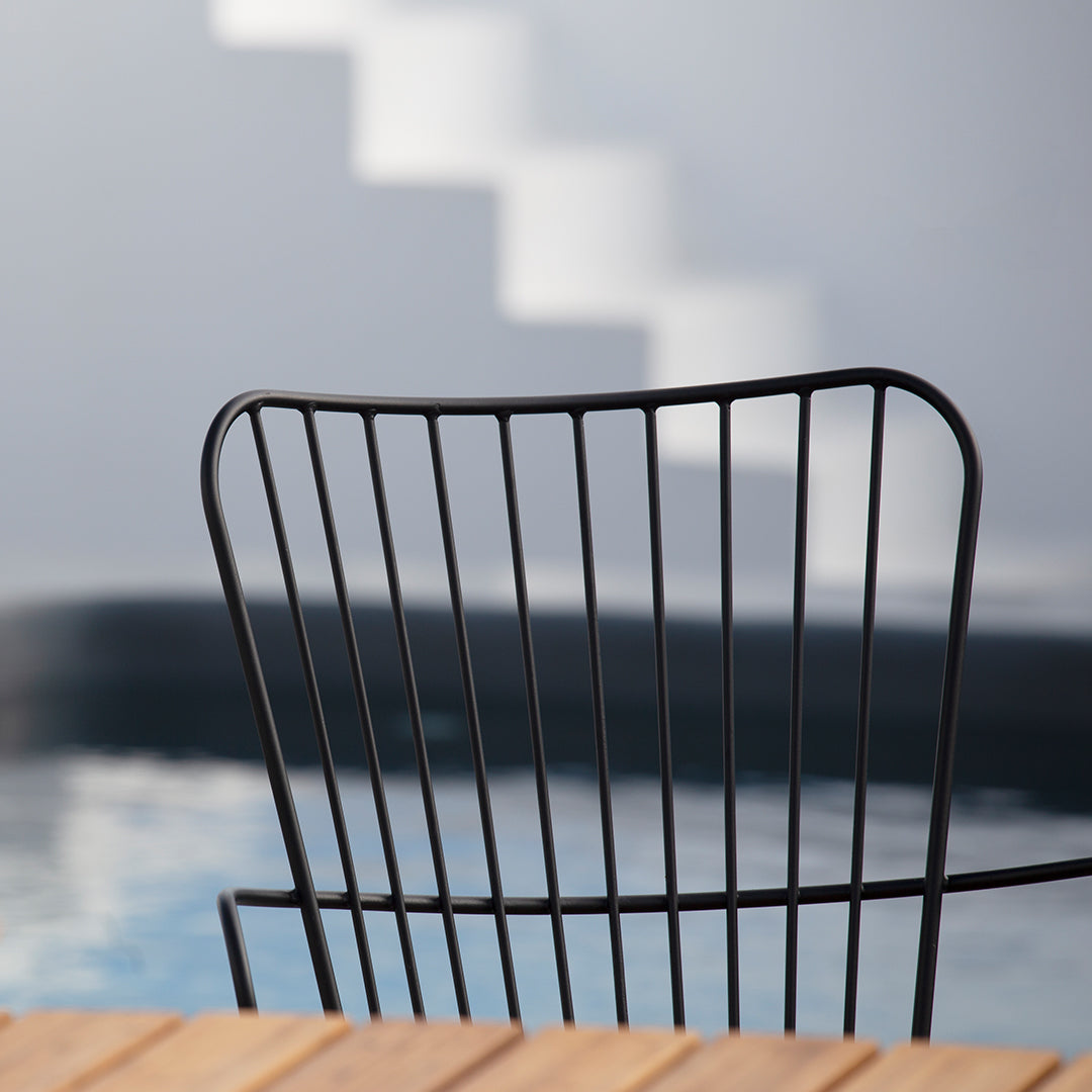 Black wire chair against a soft gray background, with a hint of blue reflection from a pool.
