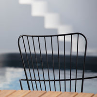 Black wire chair against a soft gray background, with a hint of blue reflection from a pool.