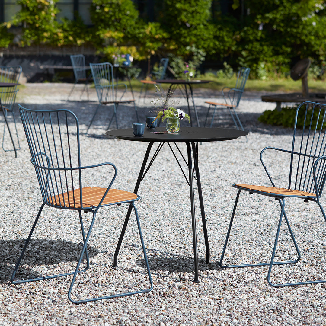 Black round table with gray metal chairs featuring wooden seats, set on a gravel outdoor surface.