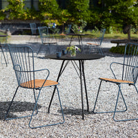 Black round table with gray metal chairs featuring wooden seats, set on a gravel outdoor surface.