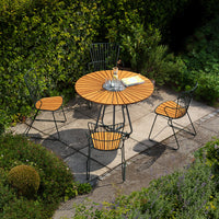 Round wooden patio table with black metal legs, surrounded by black and wooden chairs, set in a lush green garden.