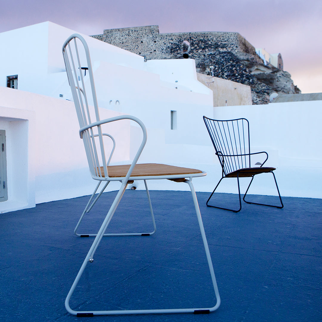 "Two modern chairs with white frames and wooden seats, set against a blue floor and whitewashed walls."