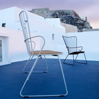 "Two modern chairs with white frames and wooden seats, set against a blue floor and whitewashed walls."